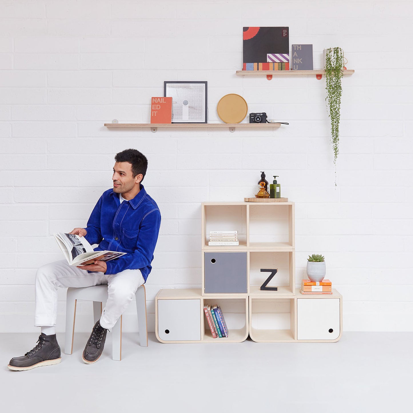 A pair of Lozi's plywood display shelves on a white brick background, with a man and storage system below