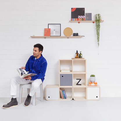 A pair of Lozi's plywood display shelves on a white brick background, with a man and storage system below