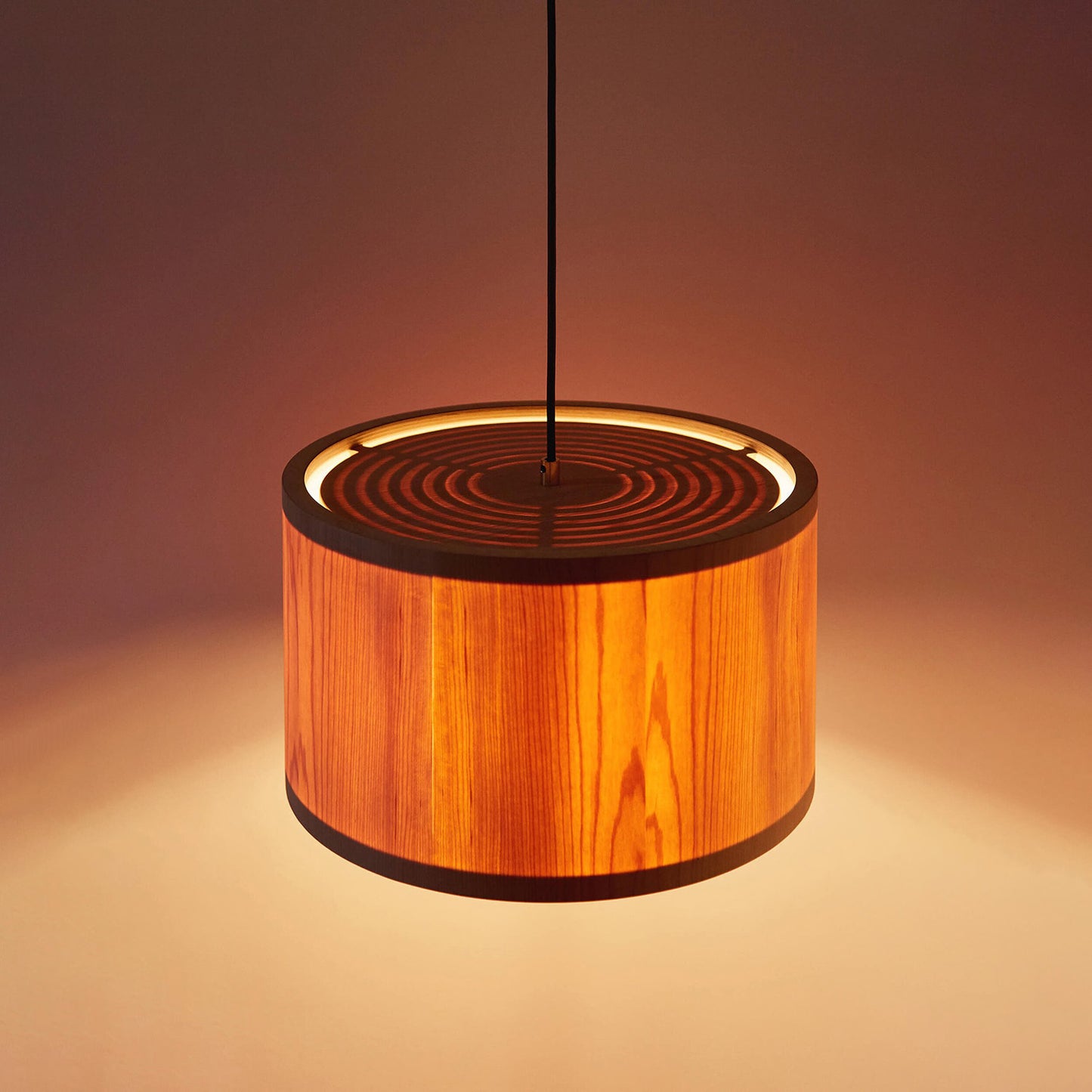 A close up of Lozi's plywood and translucent wood veneer Round Lamp turned on in a dark room