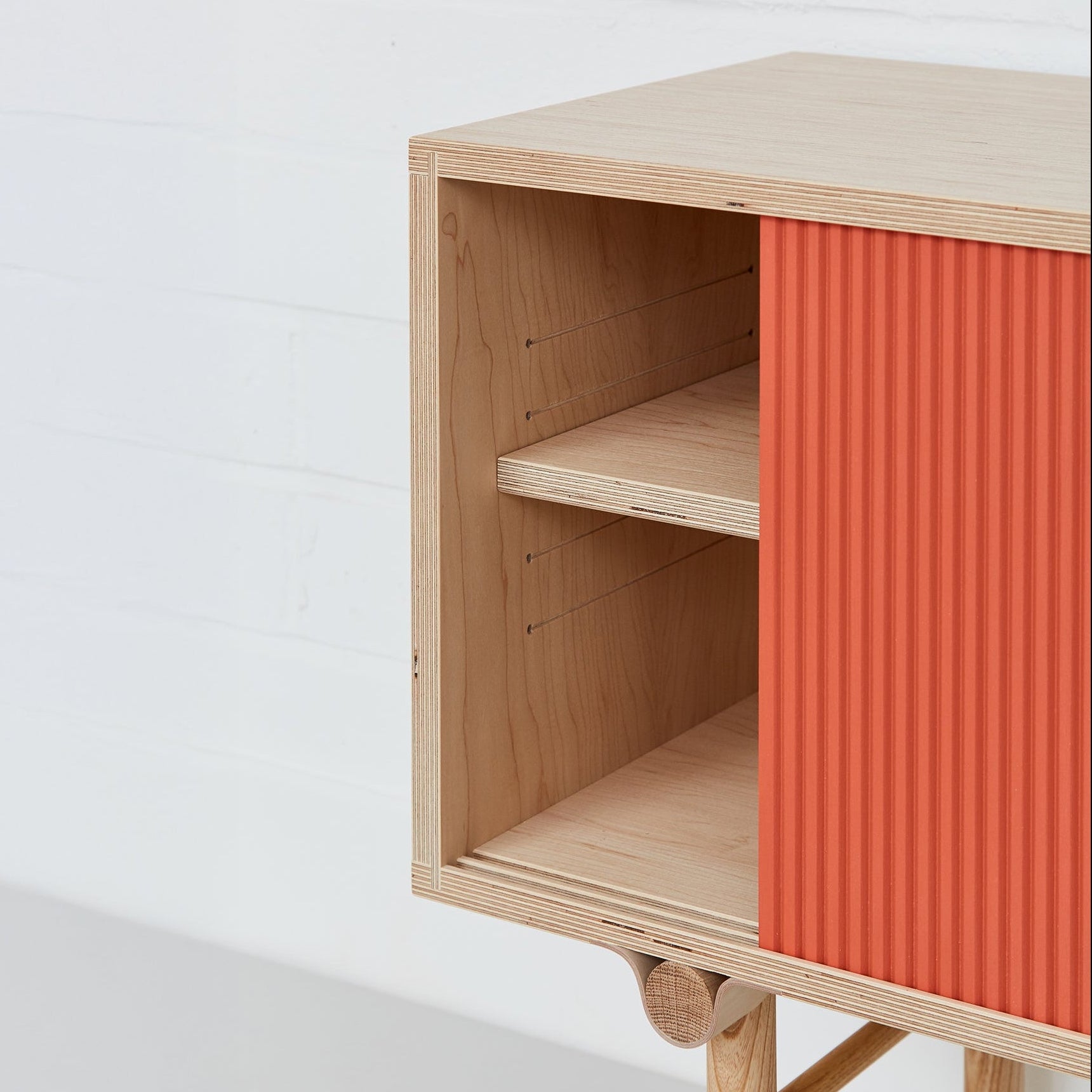 Close of detail of Lozi's birch plywood sideboard, with inside shelving with adjustable height,  with an orange corrugated panel on a white background